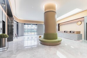 Un vestíbulo moderno con un pilar central, una recepción y un gran ventanal hacia el exterior.