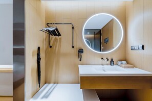 A modern bathroom with a wooden vanity, a round mirror with underglow lighting, a towel rack, and a handheld showerhead. - Ji Hotel (Shanghai)