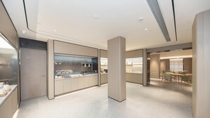 A modern kitchen with a central island, a dining area with tables, and a large pillar. - Ji Hotel (Ningbo)