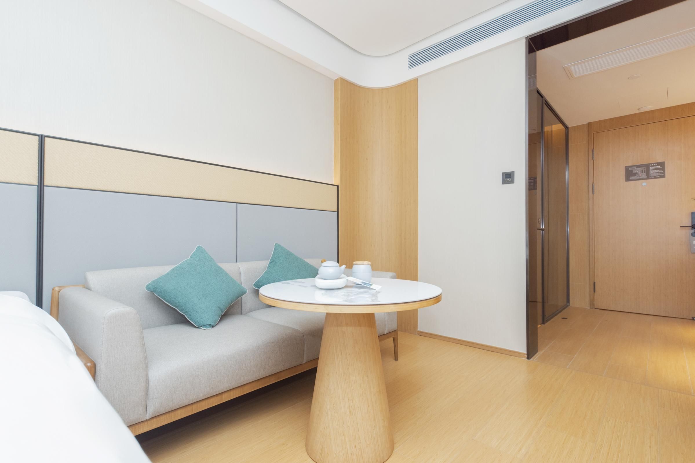 A modern hotel room with a sofa, a round table, and a wooden door.