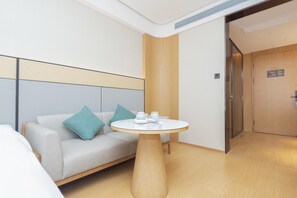 A modern hotel room with a sofa, a round table, and a wooden door. - Ji Hotel (Ningbo)