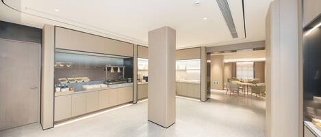 A modern kitchen with a central island, a dining area with tables and chairs, and a hallway leading to a seating area.