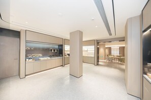 A modern kitchen with a central island, a dining area with tables and chairs, and a hallway leading to a seating area. - Ji Hotel (Ningbo)