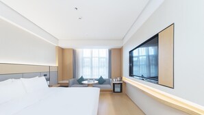 A hotel room with a large bed, a small table with chairs, a TV mounted on the wall, and a window with curtains. - Ji Hotel (Ningbo)