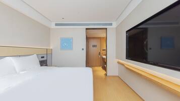 Una habitación de hotel con una cama, televisión, puerta y una pequeña lámpara de pared.