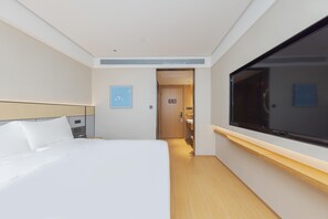 A hotel room with a bed, a television, a door, and a small wall-mounted light. - Ji Hotel (Ningbo)