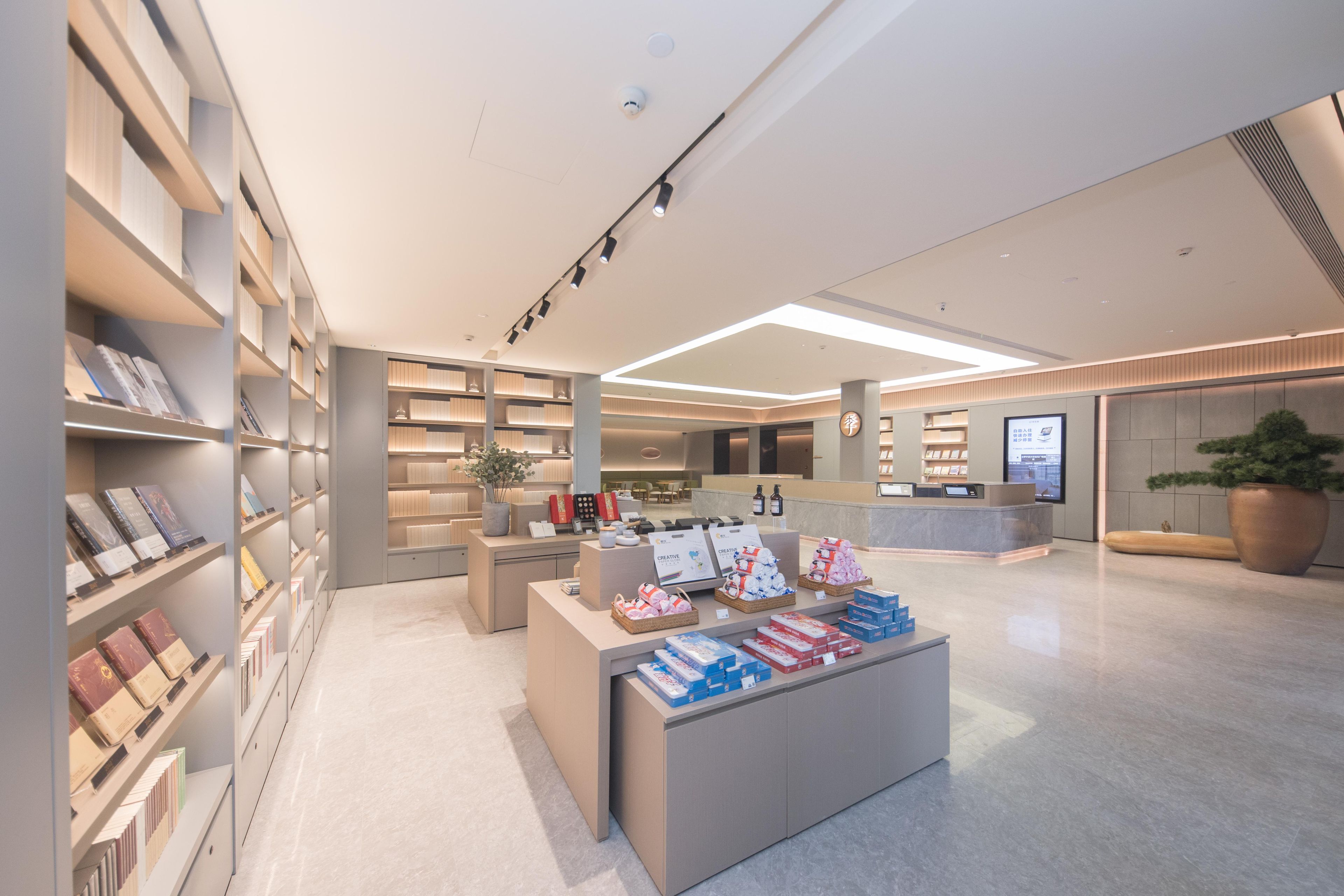A modern library interior with bookshelves, a reception desk, and a large potted plant.