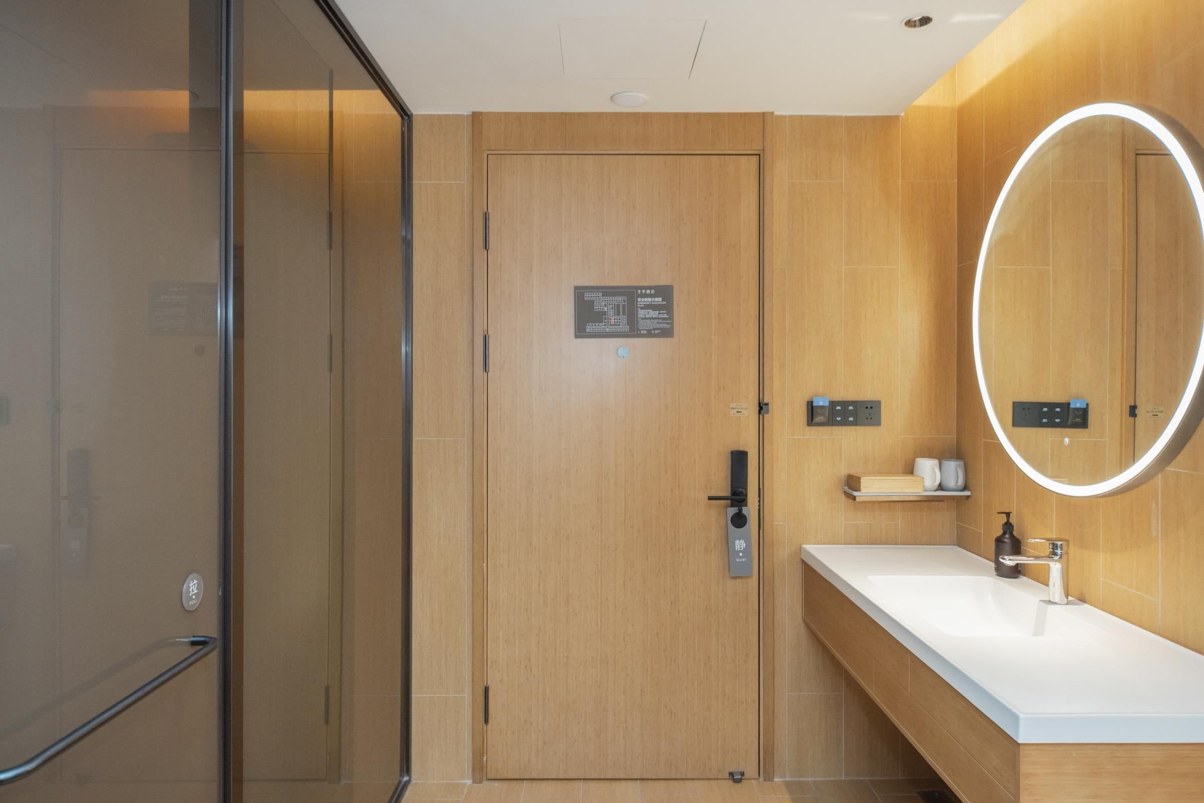 A modern bathroom with a wooden door, a mirror with a light halo, a sink, and a towel rack.