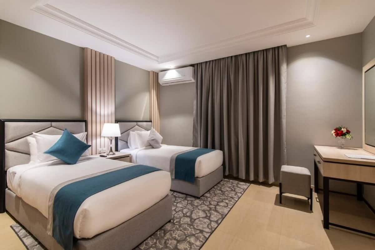 A hotel room with two beds, a desk, a chair, a lamp, and a mirror.