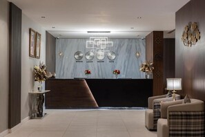 A modern reception area with a marble wall, a reception desk, and a seating area with two armchairs and a lamp. - Enala Tabuk Hotel (Tabuk)