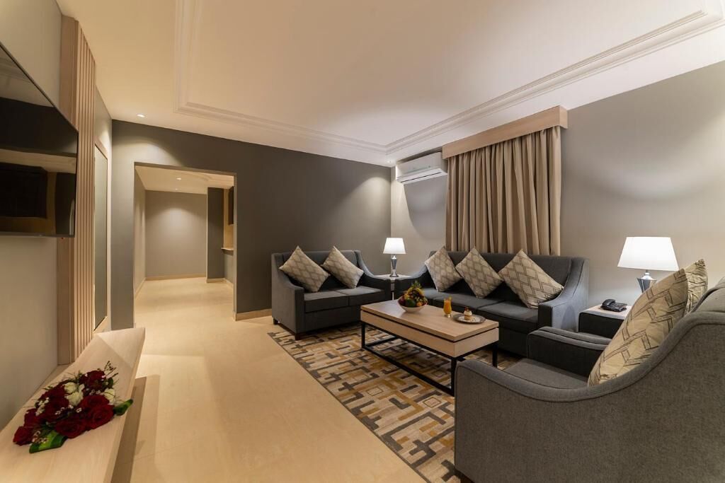A modern hotel room with a sofa set, a coffee table, and a decorative bench with flowers.