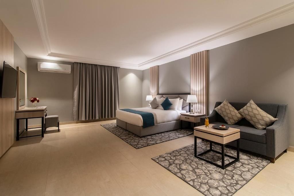 A hotel room with a bed, bedside table, lamp, sofa, and a TV.