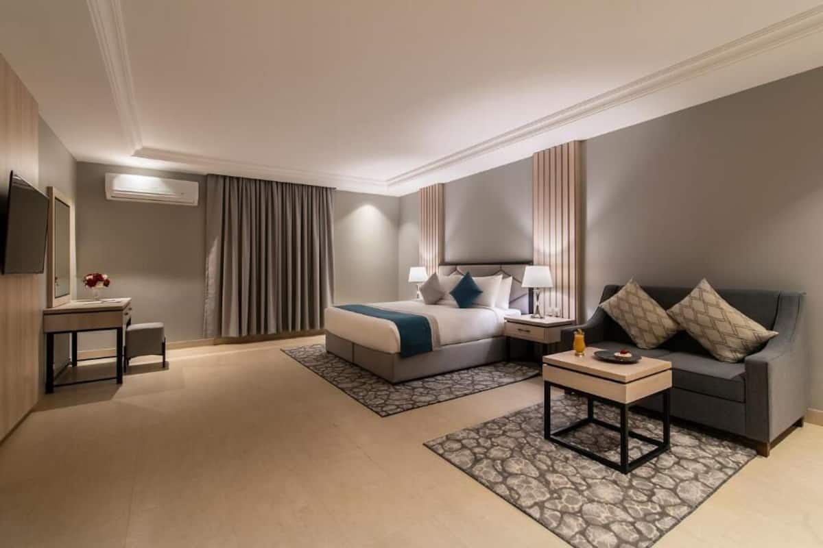 A hotel room with a bed, bedside table, lamp, sofa, and a TV.
