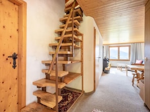 A wooden spiral staircase in a room with a carpeted floor, a window with a view, and a door with a handle.