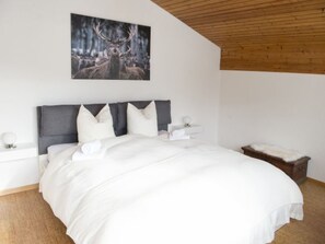 Une chambre à coucher avec un grand lit, une tête de lit, une table de chevet et une commode, ainsi qu’un tableau représentant des cerfs accroché au mur.
