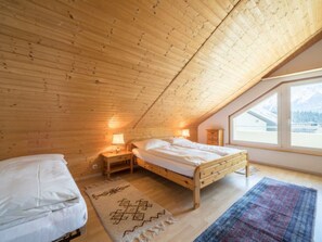 A bedroom with a wooden ceiling, two beds, a window with a view, and a rug. - Val Signina 3-28 by Interhome (Laax)