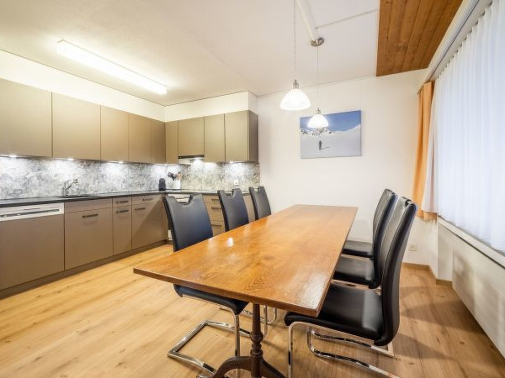A modern kitchen with wooden cabinets, a marble backsplash, and a dining area with a wooden table and black chairs.