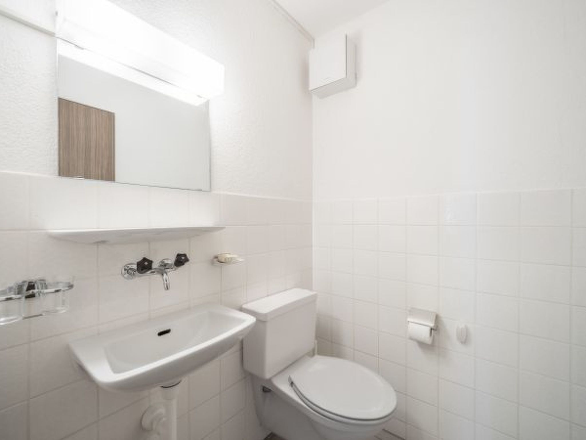 Une salle de bain avec un lavabo, des toilettes et un miroir, le tout de couleur blanche.