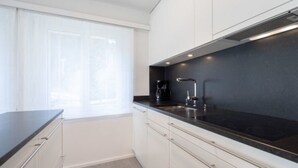 A modern kitchen with white cabinets, a black countertop, and a window with white curtains. - Val Signina 5-2 by Interhome (Laax)