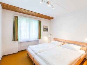 A hotel room with a double bed, a window with curtains, a wall-mounted light, and a small picture. - Val Signina 4-8 by Interhome (Laax)