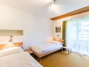 Quarto de hotel com duas camas, janela com cortinas, uma secretária e uma luminária.