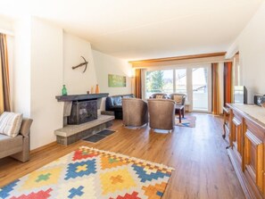 A living room with a fireplace, a sofa, a dining area with chairs, and a colorful rug. - Val Signina 4-8 by Interhome (Laax)