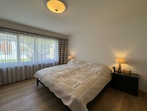 Une chambre à coucher avec un lit, deux lampes de chevet, une fenêtre avec des rideaux et un radiateur.
