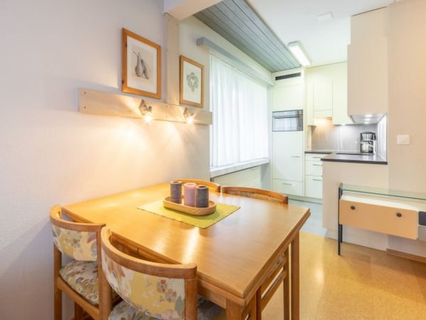 Un comedor con mesa y sillas de madera, una pequeña cocina con estufa y armarios, y cuadros en la pared.