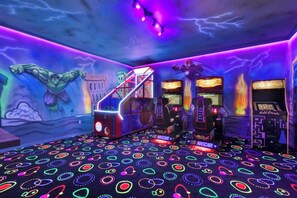 A gaming arcade with neon lights, racing game machines, and a mural of a superhero. - Windsor Island Resort Homes and Townhomes (Davenport)