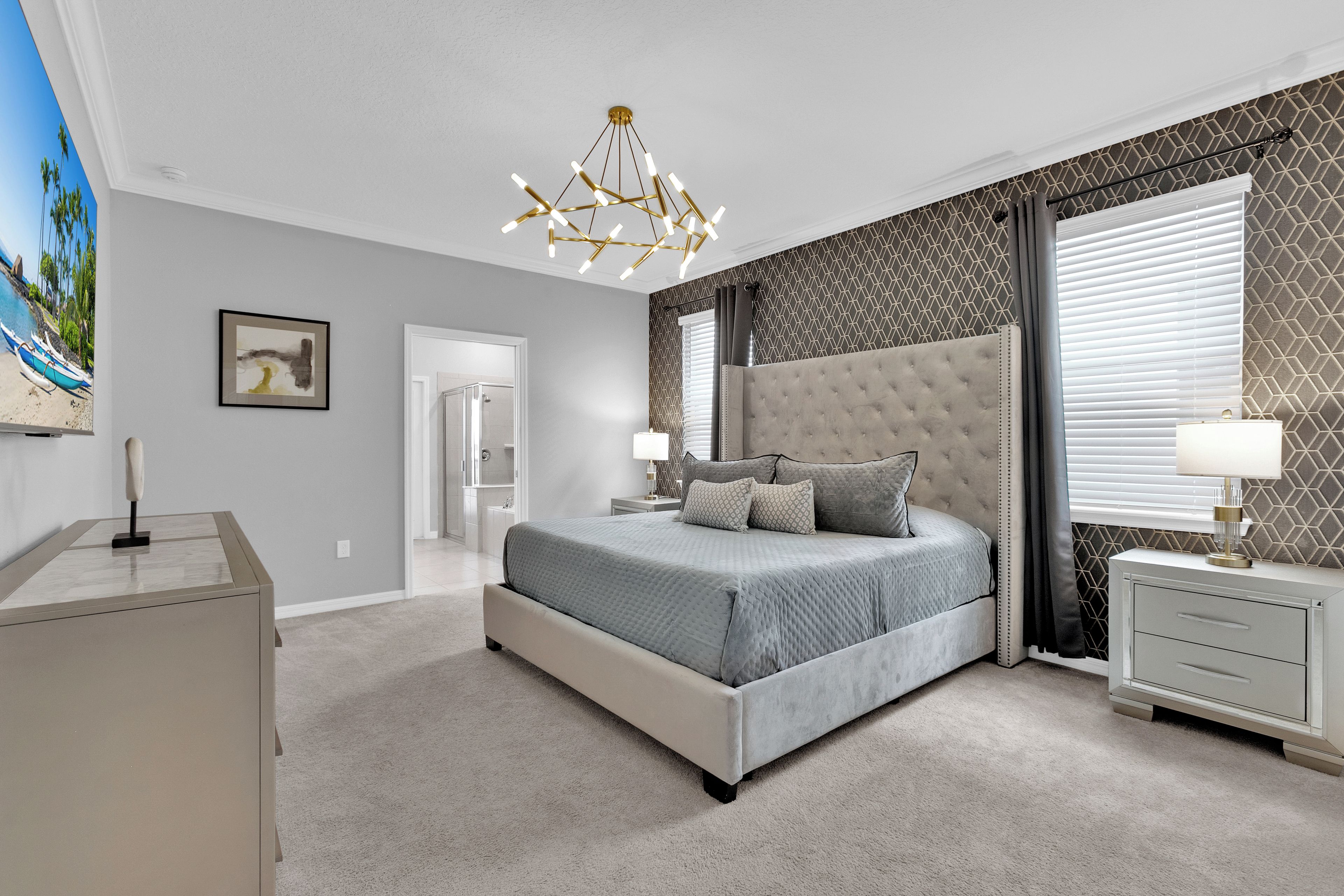 A bedroom with a large bed, a nightstand, a desk, and a painting on the wall.