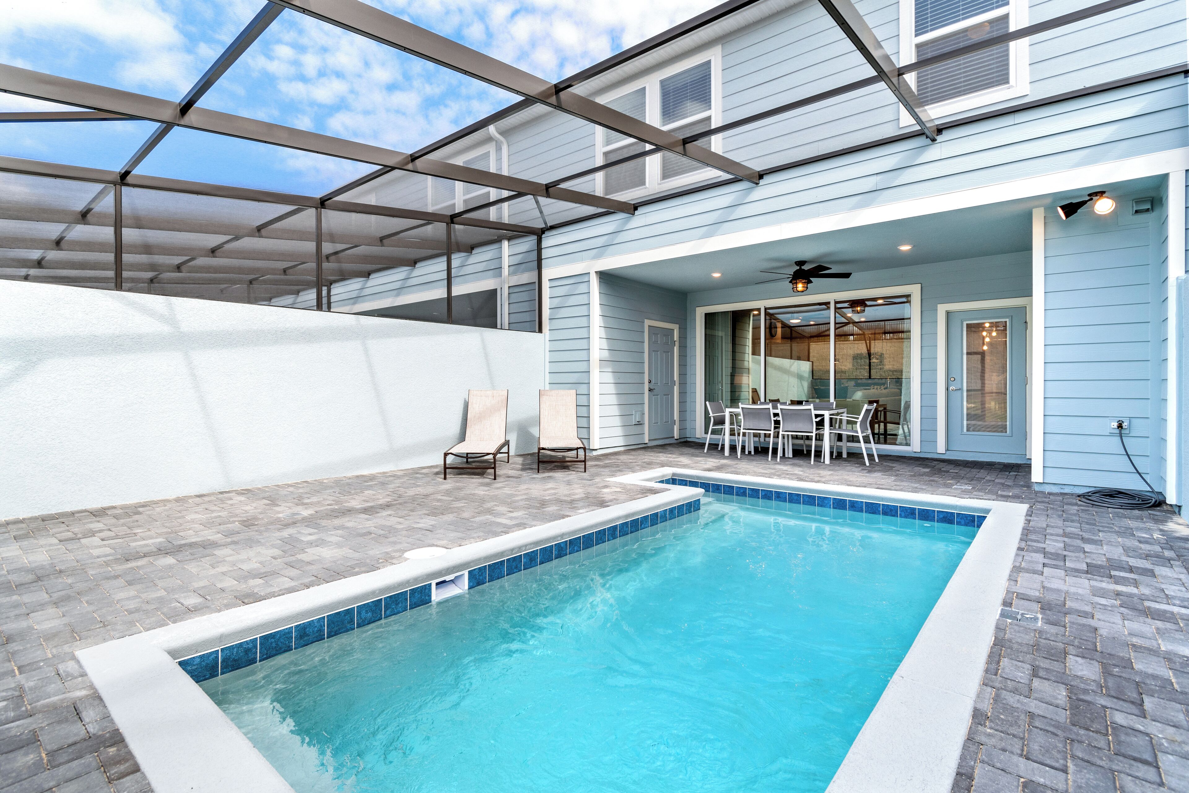 Ein Schwimmbad mit überdachter Terrasse, einem Tisch mit Stühlen und Blick auf das Haus.