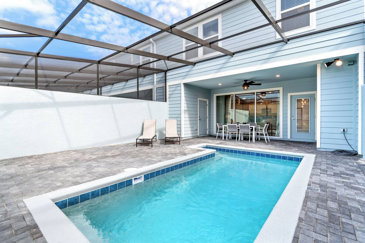 Ein Schwimmbad mit überdachter Terrasse, einem Tisch mit Stühlen und Blick auf das Haus.