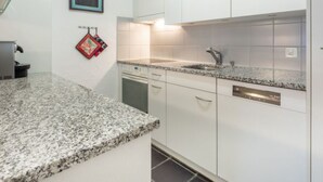 Eine Küche mit weißen Schränken, einer Granit-Arbeitsplatte, einem Geschirrspüler und einem kleinen Fenster.