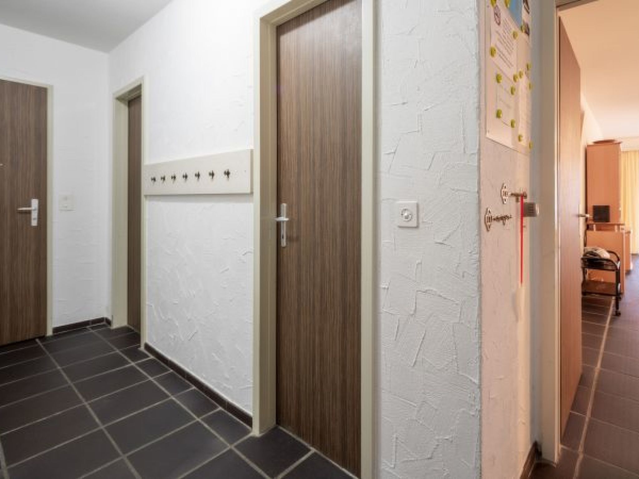 En hall med tre trädörrar, en vit, strukturerad vägg och ett klinkergolv.