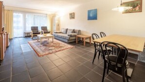 Ein modernes Wohnzimmer mit einer Couch, Sesseln, einem Esstisch und einem Teppich.