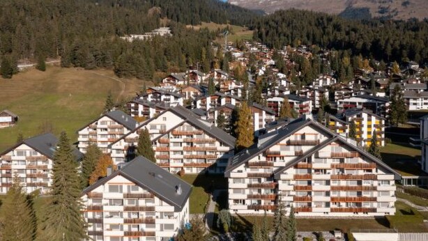 Ein Wohngebiet mit modernen mehrstöckigen Gebäuden, vermutlich Wohnungen, umgeben von viel Grün und Bergen.