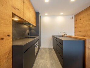A compact kitchen with wooden cabinets, a stainless steel sink, and a built-in oven. - Val Signina 7-12 by Interhome (Laax)