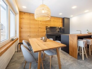 A modern kitchen with wooden cabinets, a dining table with chairs, and a hanging light fixture. - Val Signina 7-12 by Interhome (Laax)