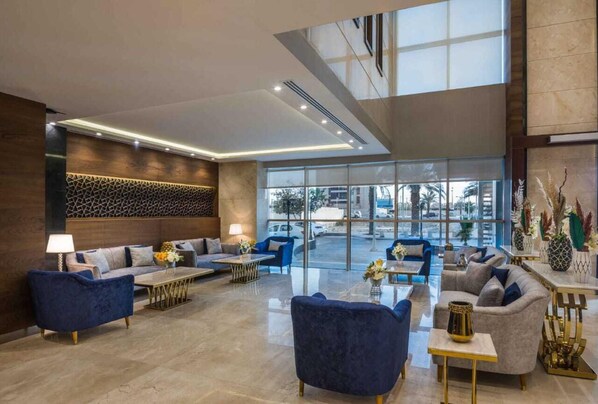 Un hall d’entrée spacieux au design moderne, comprenant un espace détente avec des canapés et des fauteuils, une table basse et un vase décoratif.