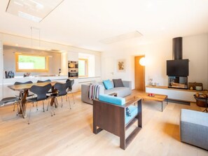 A modern living room with a sofa, coffee table, and dining area with chairs. - Casa Fau by Interhome (Laax)