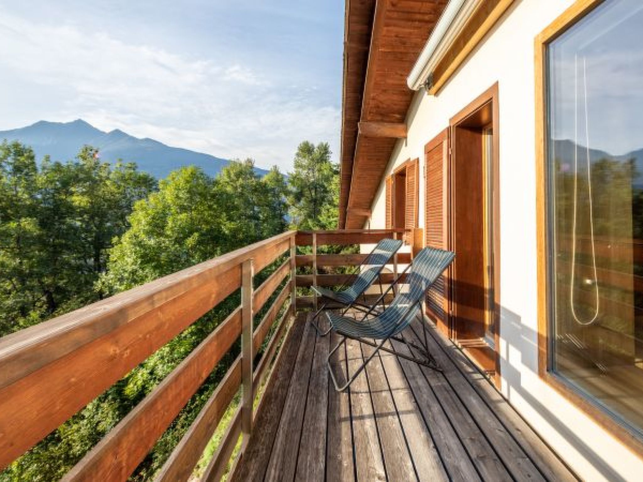 A wooden deck with two lounge chairs and a glass door.