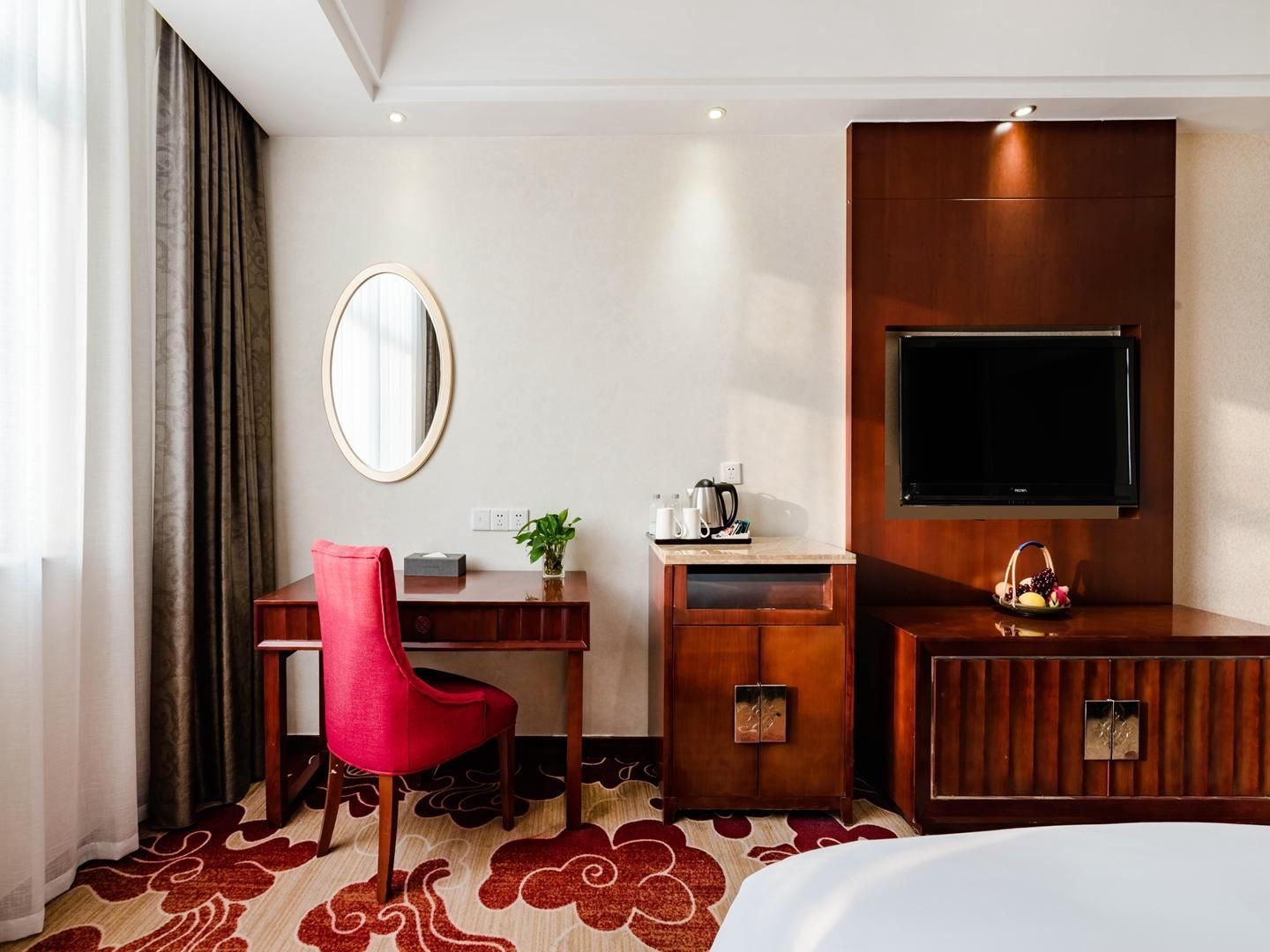 A hotel room with a bed, a desk with a chair, a TV, and a mirror.