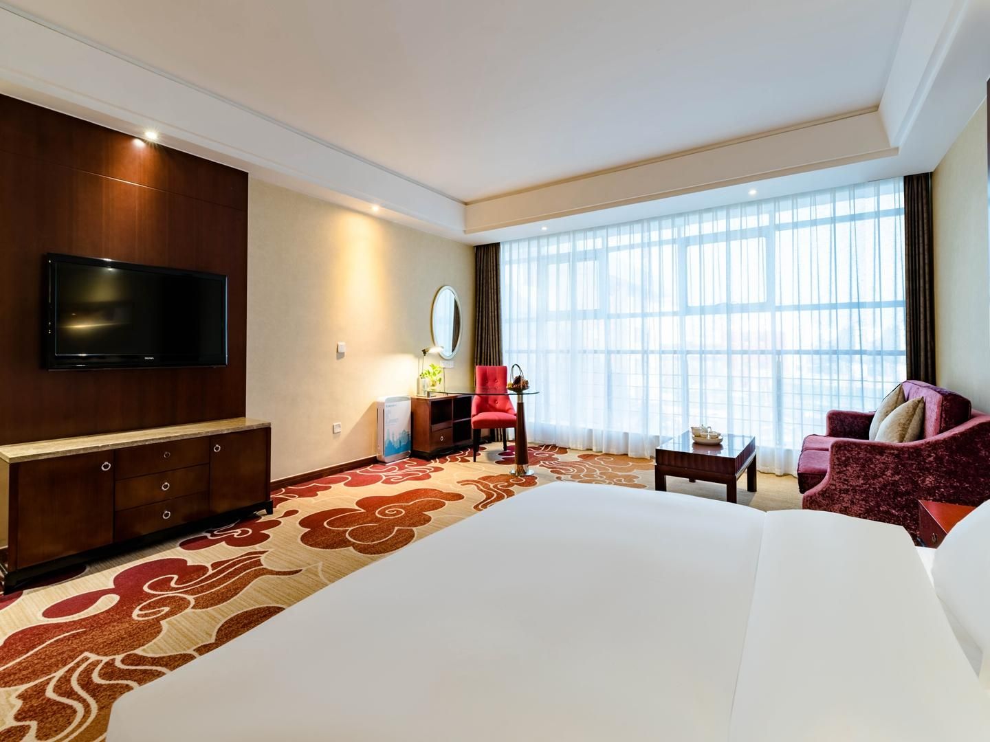 Ein Hotelzimmer mit einem großen Bett, einem Flachbildfernseher, einem Schreibtisch, einem Sessel und einer Couch.