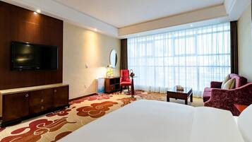 Ein Hotelzimmer mit einem großen Bett, einem Flachbildfernseher, einem Schreibtisch, einem Sessel und einer Couch.