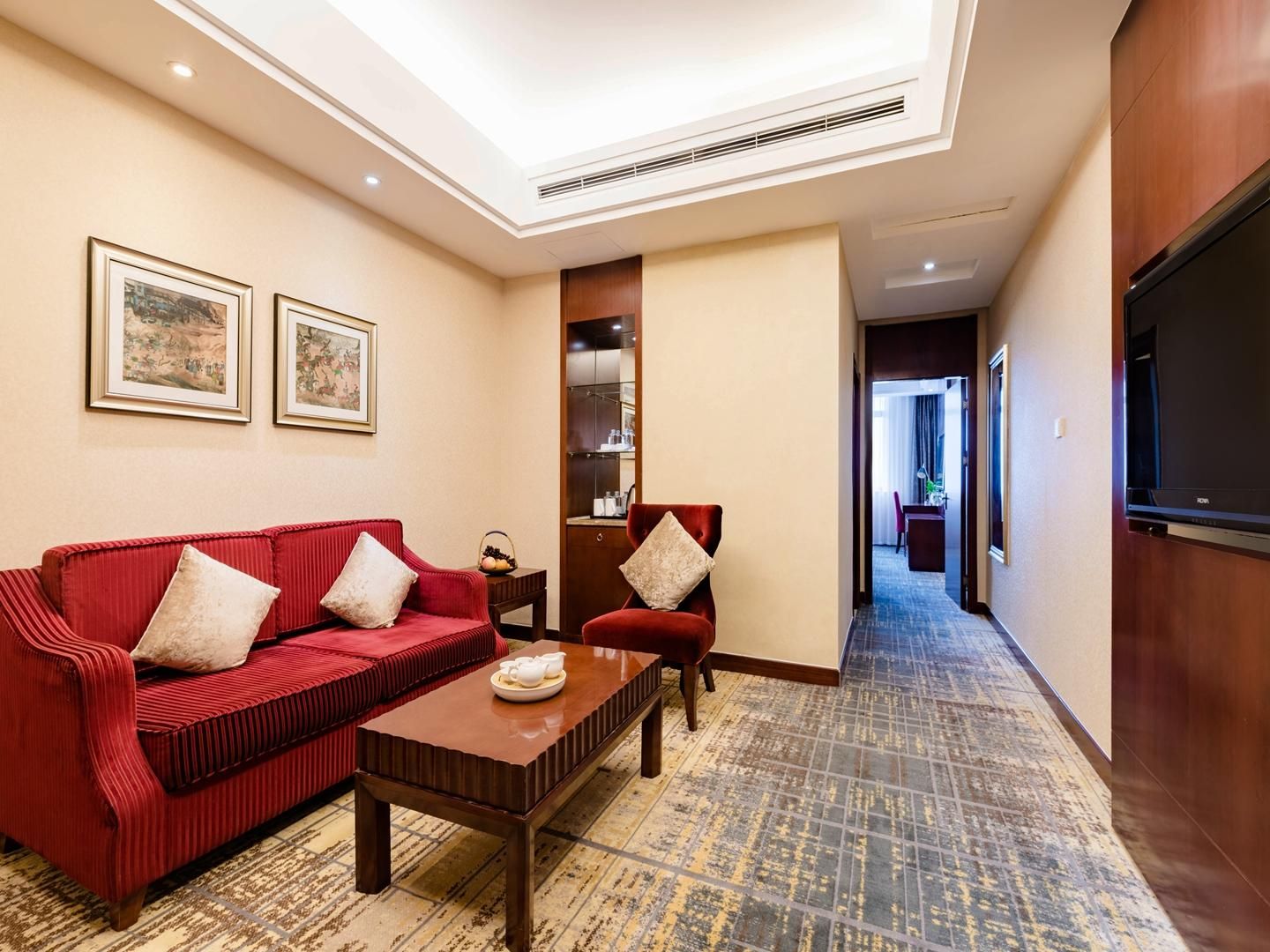 Habitación de hotel con un sofá rojo, una mesa de centro de madera, un televisor y cuadros en la pared.