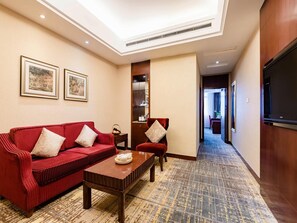 Quarto de hotel com sofá vermelho, mesa de centro de madeira, televisão e quadros nas paredes.