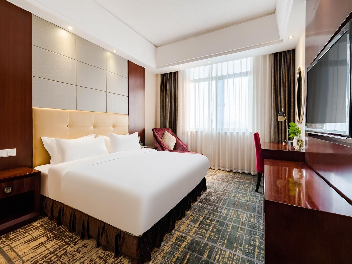 A hotel room with a large bed, a desk, a chair, and a TV.