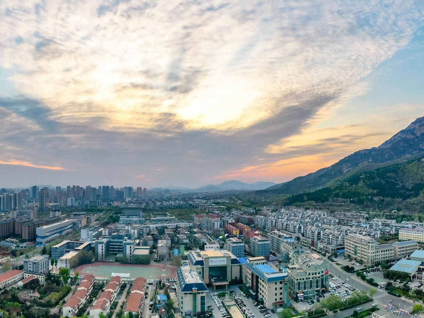 A cityscape with modern buildings, a large open square, and a mountain in the background.