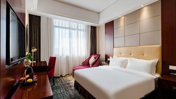 A hotel room with a large bed, a desk with a TV, a chair, and a window with curtains.