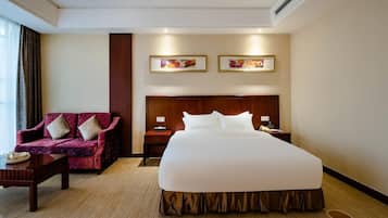 A hotel room with a large bed, a sofa, a nightstand, and two framed pictures on the wall.